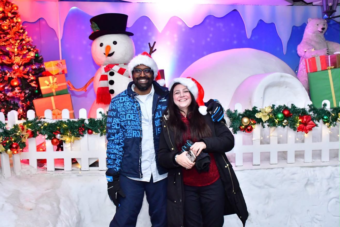 Rusul and Ashir in Santa hats in front of a snowy Christmas scene